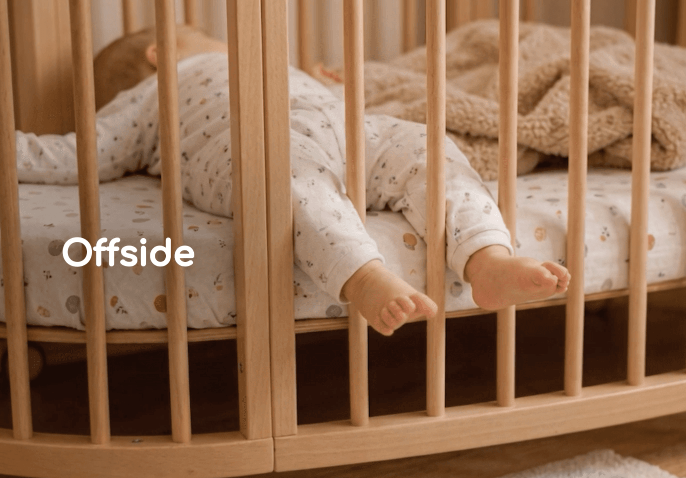 A baby sleeping with their feet extending through the bars of a cot beside the word Offside